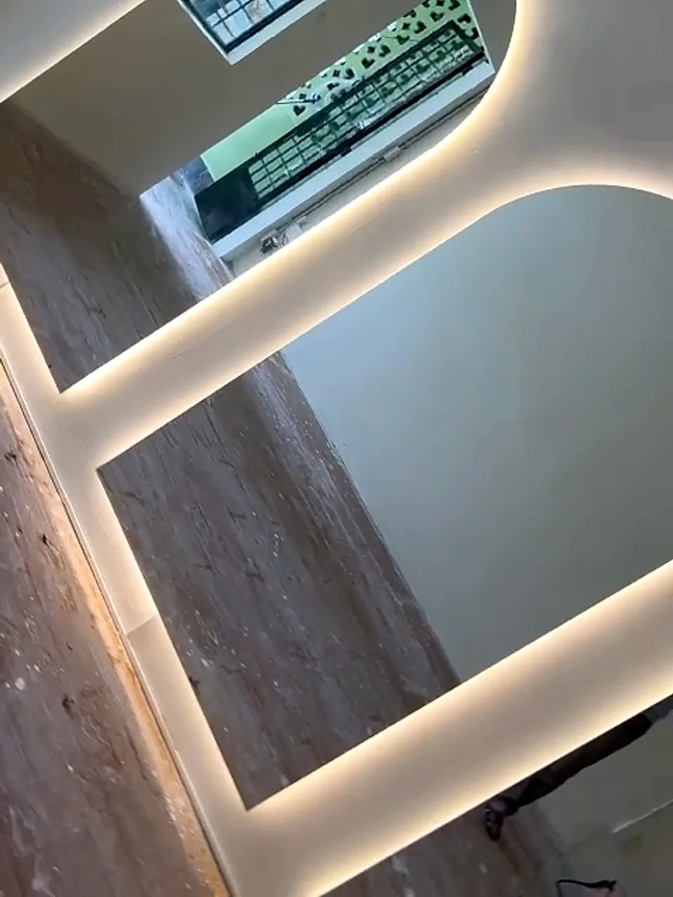 Cận cảnh cạnh tấm gương soi bo vòm và dải đèn LED hắt sáng viền tại công trình CMT8, mặt gương phản chiếu ô cửa và ánh sáng, thể hiện độ hoàn thiện mượt của đường bo cong và mối ghép sát tường