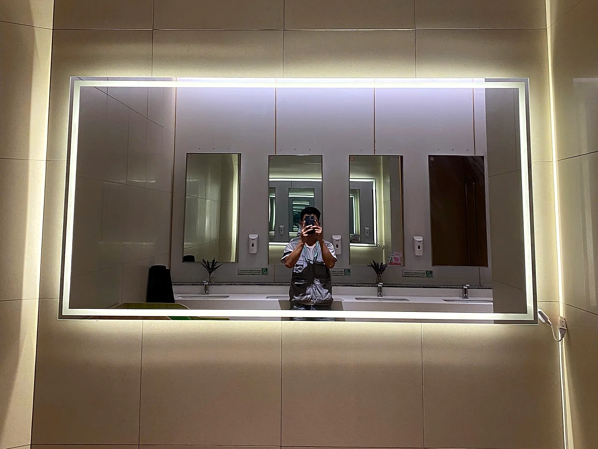 Gương soi nhà vệ sinh TTTM PARC MALL với gương cường lực dày 8mm viền đèn LED, bề mặt phẳng phản chiếu rõ nét lắp phía trên quầy lavabo đá, thể hiện tiêu chuẩn kỹ thuật và an toàn cho gương công cộng