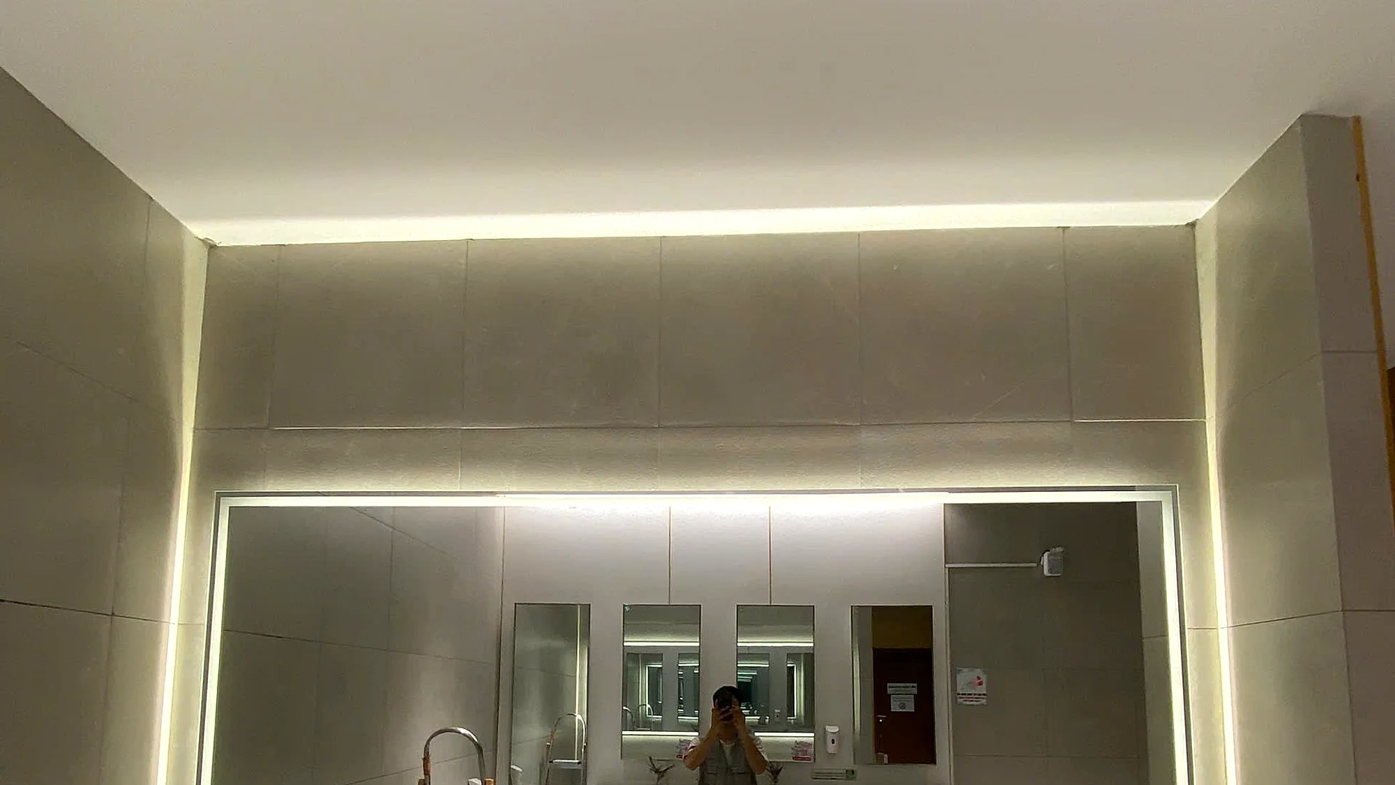 Gương LED khổ lớn đã thi công hoàn thiện tại nhà vệ sinh TTTM PARC MALL Tạ Quang Bửu TP.HCM, viền đèn LED hắt sáng ấm, tường ốp đá khổ lớn, quầy lavabo đôi, không gian sạch sẽ sang trọng