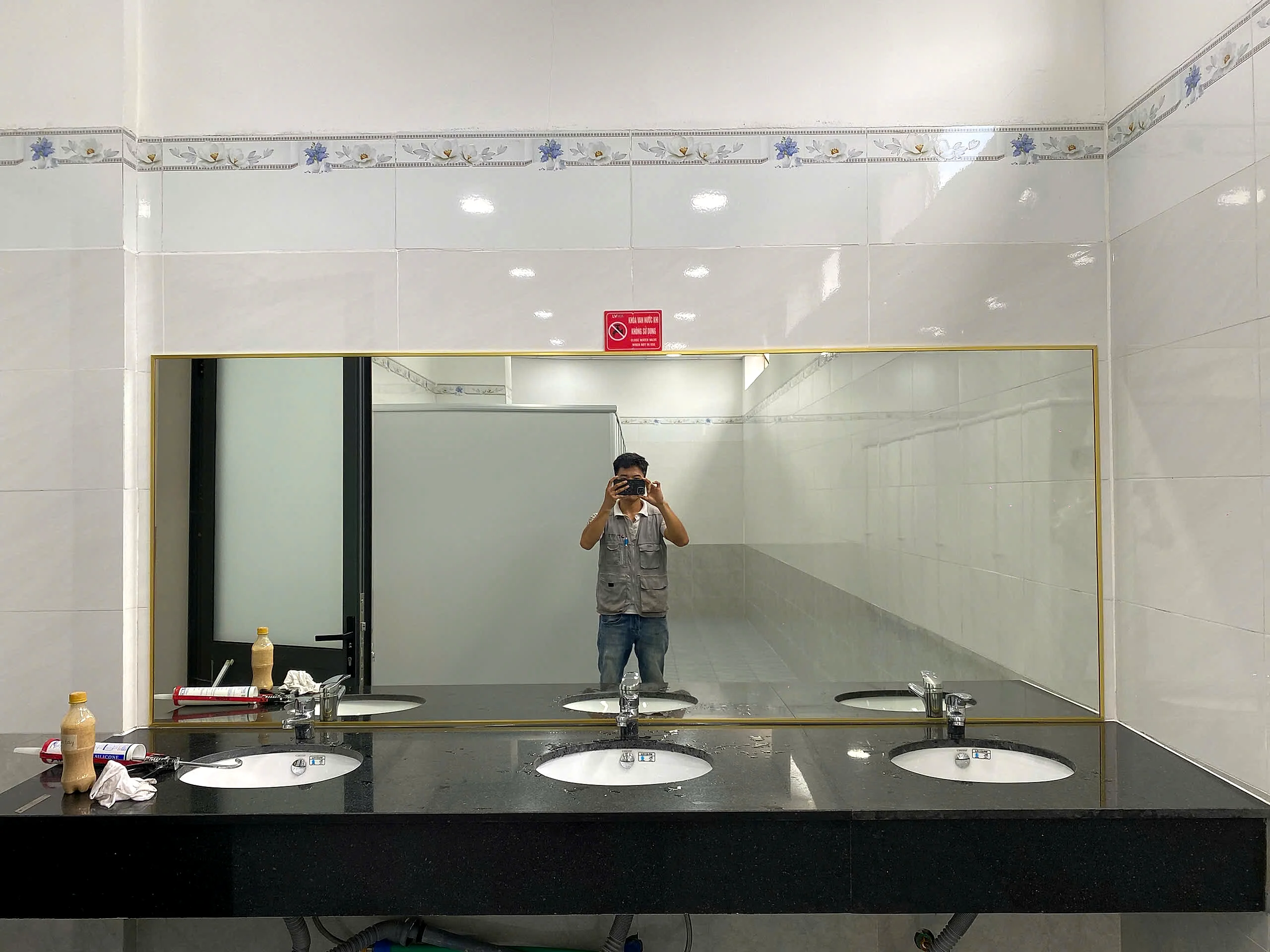 Gương WC khổ lớn khung nhôm vàng lắp cho khu vệ sinh nhiều lavabo tại Đồng Nai, mặt gương phẳng phản chiếu rõ, bàn đá granite đen
