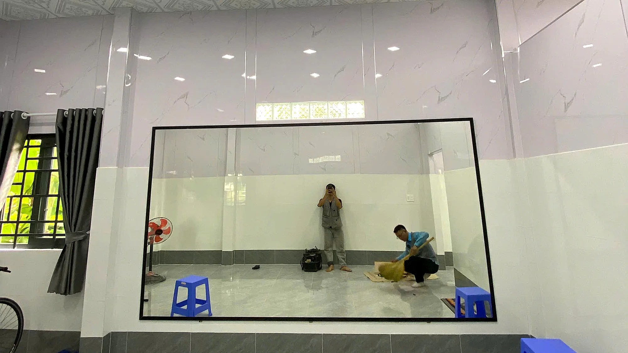 Tấm gương soi khổ lớn khung mảnh đã thi công lắp đặt hoàn thiện trên tường nhà, phản chiếu toàn bộ không gian phòng sáng rộng, ảnh công trình thực tế đo cắt và lắp đặt tận nơi