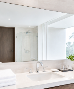 gương phòng tắm khách sạn trên bàn đá trắng với khăn gấp gọn và gạch be sáng