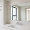 Gương phòng tắm chữ nhật phía trên lavabo trắng, gạch xám sáng và ánh sáng tự nhiên
