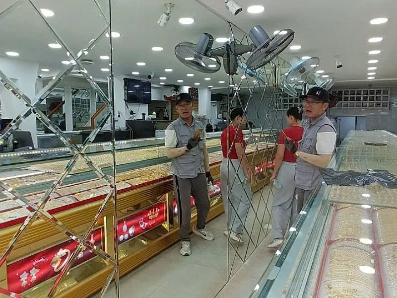 Xưởng Gương Bình Dương: Gương Cho Nhà Xưởng, Căn Hộ, Khách Sạn 11 Hai thợ đang lắp gương ghép hình thoi trên tường tiệm vàng, quầy trưng bày phía trước