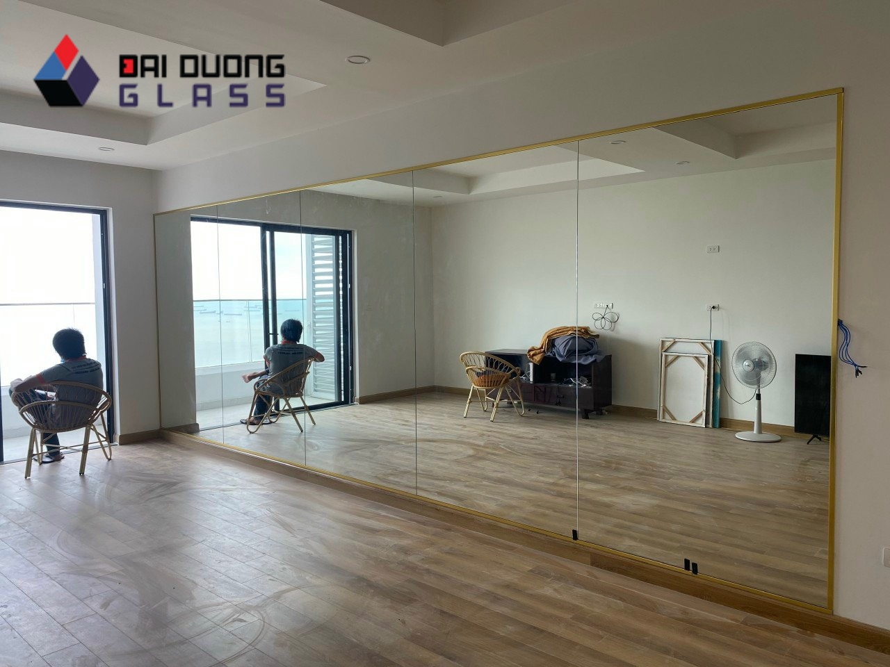 Gương soi khổ lớn viền vàng chạy dài bức tường phòng khách, phản chiếu cửa ban công